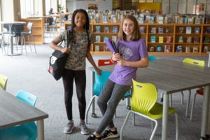 Two seventh-grade students pose for a photo with their notebooks in the library.